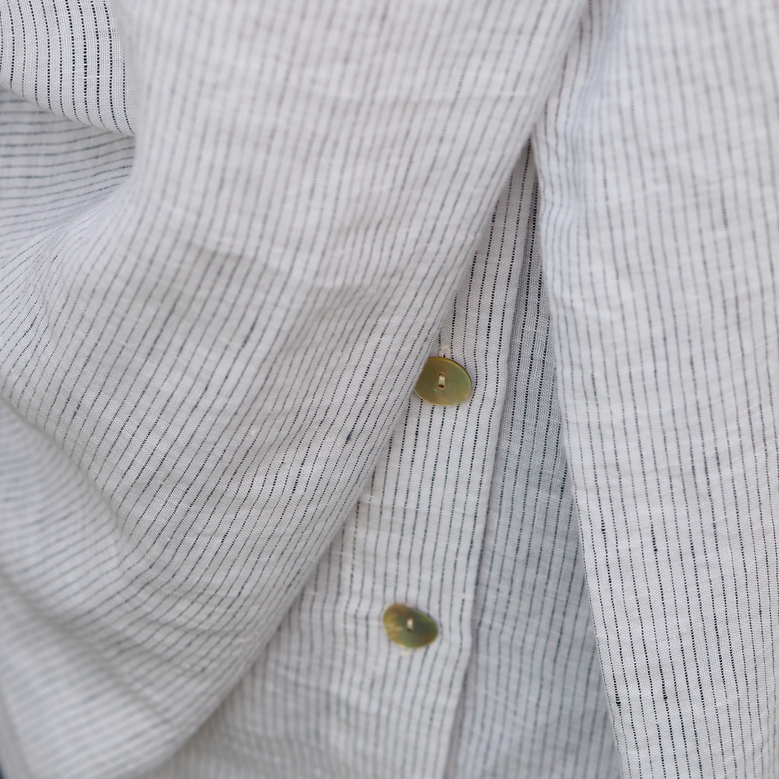 Close up of natural shell buttons and white striped 100% sustainable linen fabric. 